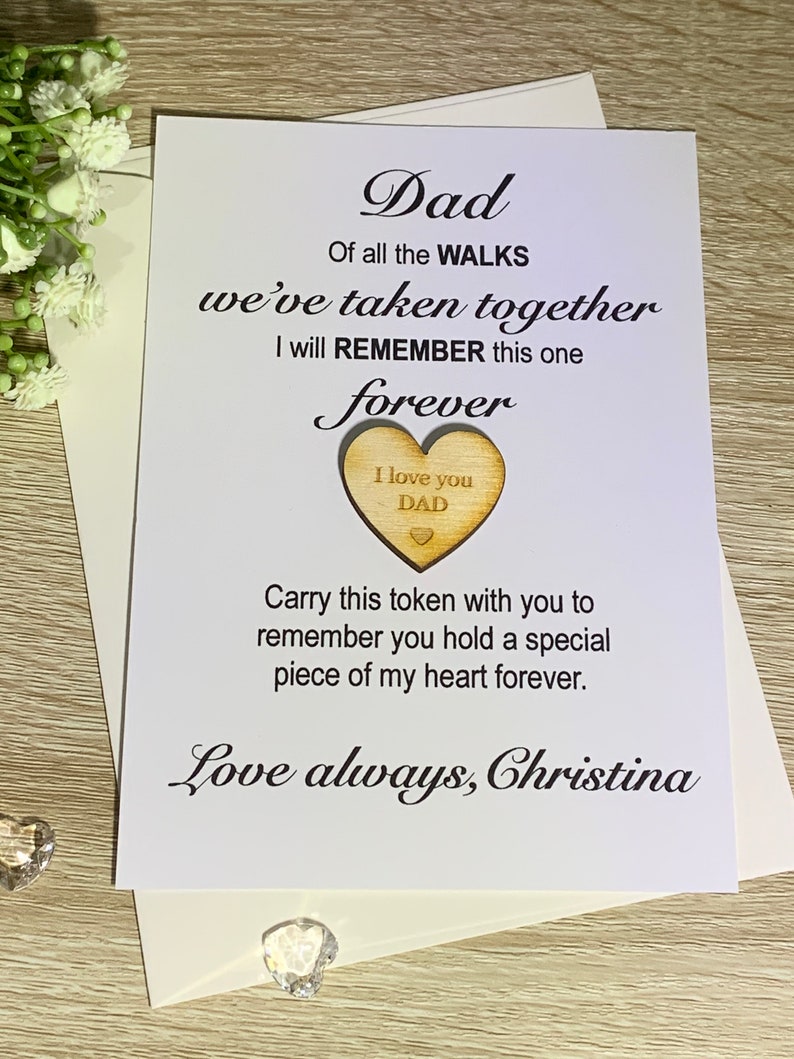 May include: A white card with black text that reads "Dad, Of all the WALKS we've taken together I will REMEMBER this one forever." A wooden heart with the text "I love you DAD" is attached to the card. The card is signed "Love always, Christina."