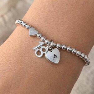 May include: Silver beaded bracelet featuring heart-shaped charms. One charm has the letter "A" and the other has the number "18". The bracelet also has two heart-shaped beads.