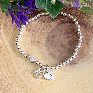 May include: Silver beaded bracelet with a charm that says "16" and a heart charm with the letter "A" engraved on it.