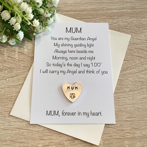 May include: A white card with a poem about a mother being a guardian angel. The card has a silver heart charm with the word "MUM" and an angel design.