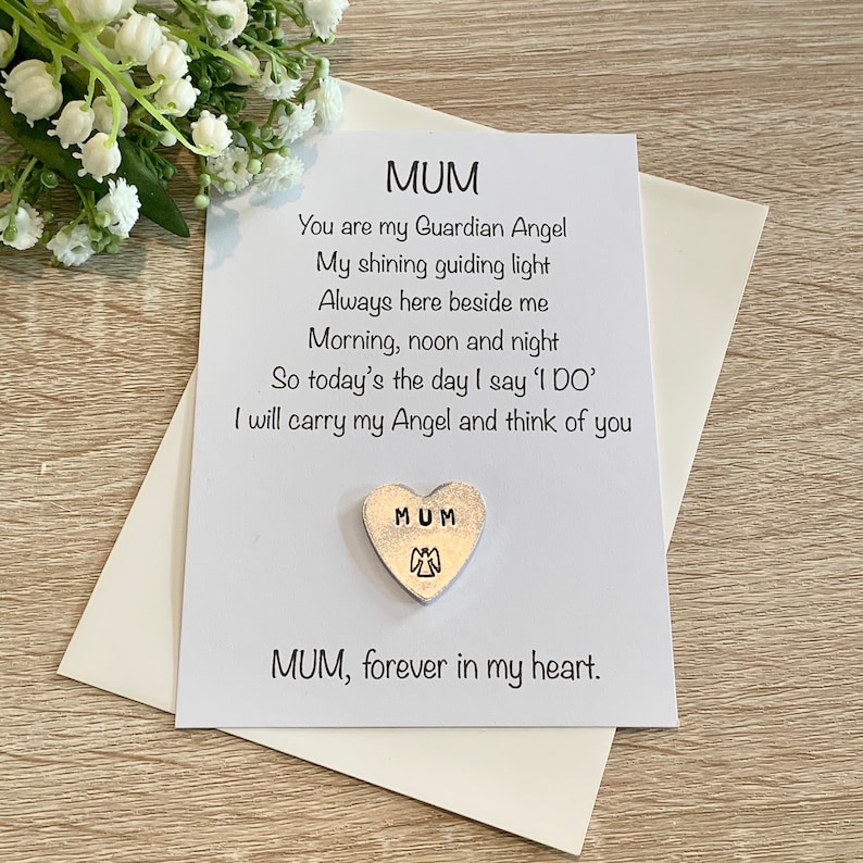 May include: A white card with a poem about a mother being a guardian angel. The card has a silver heart charm with the word "MUM" and an angel design.