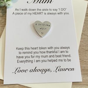 May include: A white card with a silver heart charm attached. The card reads "As I walk down the aisle to say 'I DO' A piece of my HEART is always with you." The heart charm reads "I love you MUM" and has a small heart at the bottom. The card is signed "Love always, Lauren".
