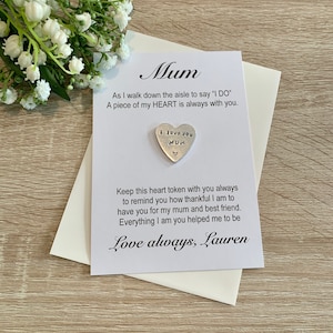 May include: A white card with the text "Mum" in cursive. The card says "As I walk down the aisle to say 'I DO' A piece of my HEART is always with you."  A silver heart charm with the text "I love you MUM" is attached to the card. The card also says "Keep this heart token with you always to remind you how thankful I am to have you for my mum and best friend. Everything I am you helped me to be Love always, Lauren."