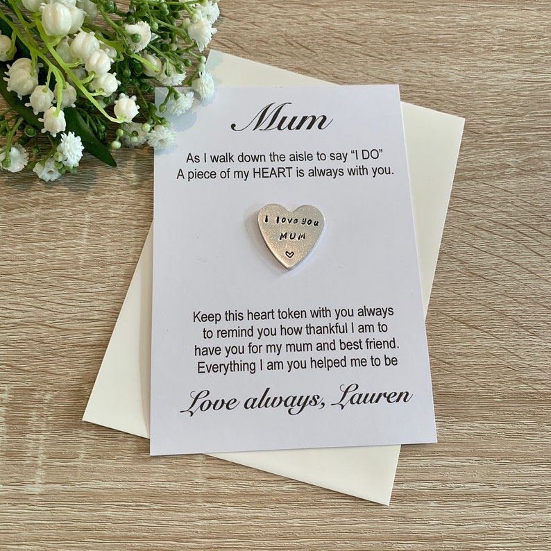 May include: A white card with the text "Mum" in cursive. The card says "As I walk down the aisle to say 'I DO' A piece of my HEART is always with you."  A silver heart charm with the text "I love you MUM" is attached to the card. The card also says "Keep this heart token with you always to remind you how thankful I am to have you for my mum and best friend. Everything I am you helped me to be Love always, Lauren."