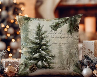 May include: A square throw pillow featuring a printed winter scene with a snow-covered evergreen tree, pine branches, and pinecones. The background includes faint, cursive script text overlaid on a soft, muted forest landscape.