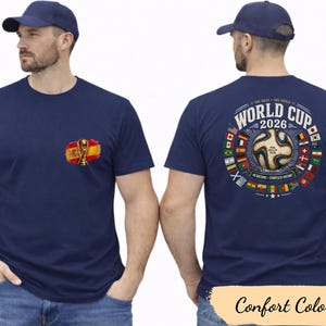 May include: Navy blue t-shirt featuring a Spanish flag and trophy graphic on the front. The back displays a World Cup 2026 design with a soccer ball and flags. The shirt is labeled "Comfort Colors".