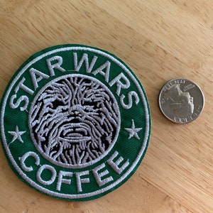 May include: A green and white embroidered patch with the text "STAR WARS COFFEE" and a stylized image of Chewbacca's face in the center.