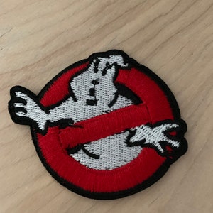 May include: A red and black embroidered patch with a white ghost in the center. The ghost is crossed out with a red line. The patch is a popular symbol from the Ghostbusters movie franchise.