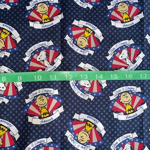 May include: A blue fabric with a repeating pattern of red, white, and blue stars and stripes. The pattern features a cartoon character with a yellow shirt and black hair. The text "Stars & Stripes" and "Forever" is repeated throughout the pattern.