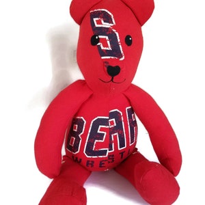 K&ouml;nnte beinhalten: Roter Pl&uuml;schteddyb&auml;r mit schwarzer Nase und Augen. Der B&auml;r tr&auml;gt ein rotes Shirt mit dem Aufdruck "BEAR WRESTLING" in Schwarz und Wei&szlig;.