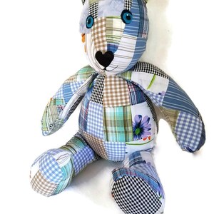 May include: A patchwork teddy bear made from blue, green and brown fabric. The bear has large blue eyes and a black heart-shaped nose.
