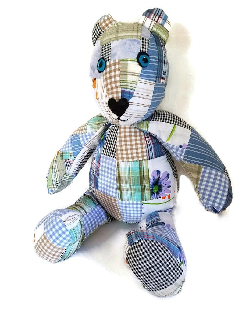 K&ouml;nnte beinhalten: Ein Patchwork-Teddyb&auml;r aus blauem, gr&uuml;nem und braunem Stoff. Der B&auml;r hat gro&szlig;e blaue Augen und eine schwarze herzf&ouml;rmige Nase.