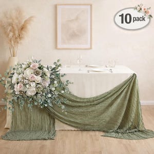 May include: A table setting with a white tablecloth, adorned with a cascading sage green fabric runner. A floral arrangement of white, pink, and green flowers and foliage decorates the table. A framed artwork hangs on the wall. The image includes a "10 pack" label.