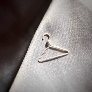 Close up of a sterling silver handmade coat hanger on a grey lapel