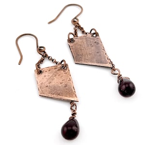 May include: A pair of copper earrings with a hammered diamond-shaped pendant and a dangling garnet gemstone.