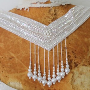 May include: White beaded necklace with a V-shaped design and a fringe of pearls.