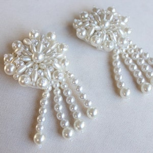 May include: A pair of white pearl earrings with a flower-shaped design and dangling pearl strands.