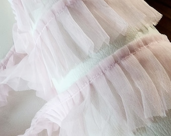 May include: Pink ruffled tulle trim, a delicate and soft fabric with a layered design. This trim is perfect for adding a touch of elegance to any project.
