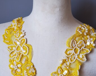 May include: Yellow lace trim with pearl and sequin embellishments. The trim features a floral design and is perfect for adding a touch of elegance to any garment.