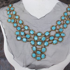 May include: A turquoise and gold beaded necklace with a V-shaped design. The necklace is made of small, round beads and larger, oval-shaped turquoise stones.