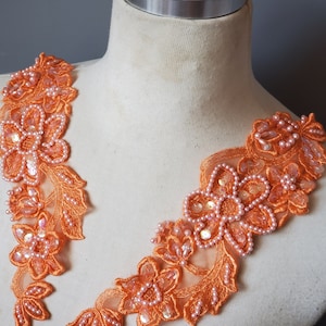 May include: Two orange lace appliques with pearl and sequin embellishments. The appliques are shaped like floral designs and are perfect for adding a touch of elegance to any garment.