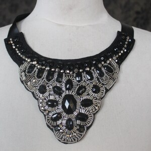 May include: A black choker necklace with silver and black bead embellishments. The necklace is in the shape of a V and has a large, central, black gemstone.