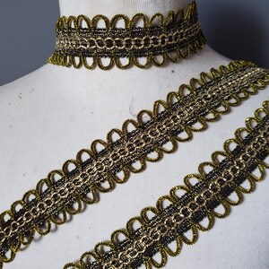 Puede incluir: Primer plano de un ribete decorativo dorado y negro y un choker a juego. El ribete presenta un borde festoneado y un dise&ntilde;o en forma de cadena. El choker es una versi&oacute;n m&aacute;s peque&ntilde;a del ribete. Los art&iacute;culos se muestran en un maniqu&iacute; blanco.