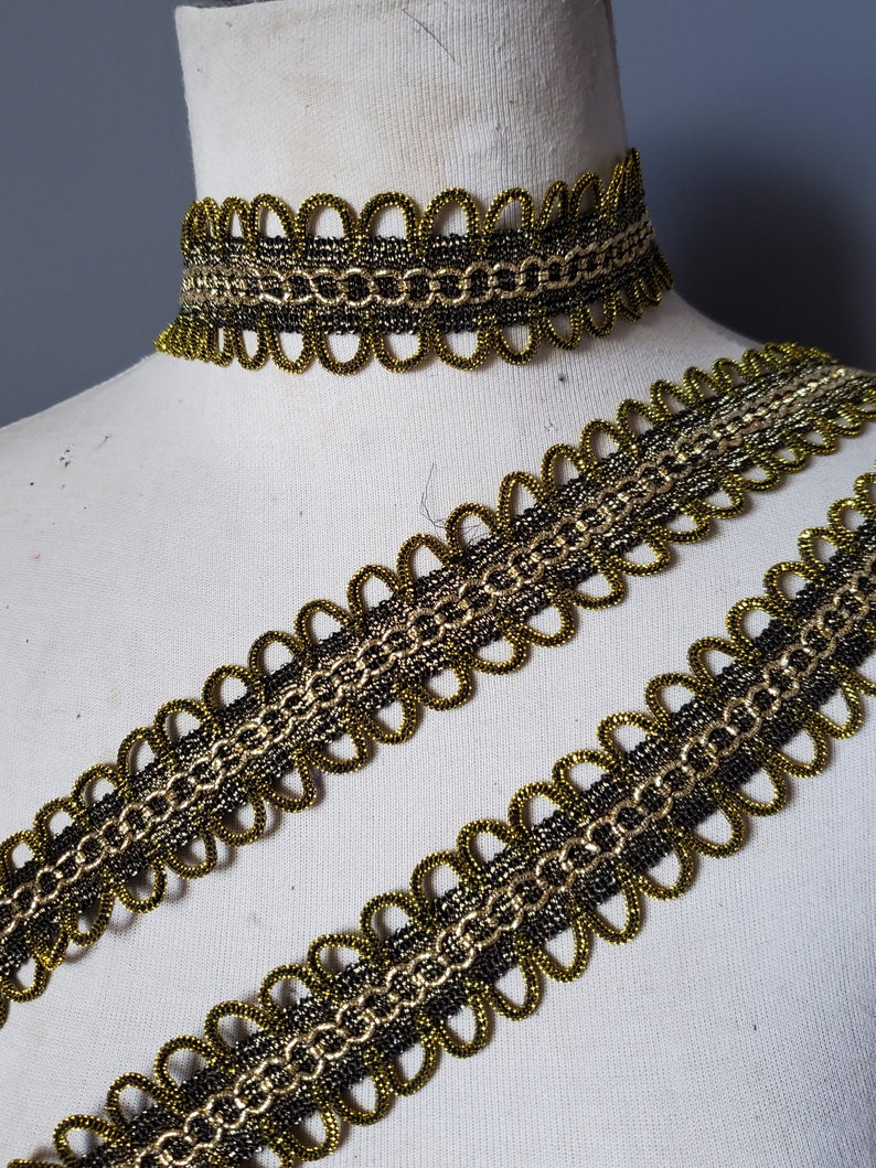 Puede incluir: Primer plano de un ribete decorativo dorado y negro y un choker a juego. El ribete presenta un borde festoneado y un dise&ntilde;o en forma de cadena. El choker es una versi&oacute;n m&aacute;s peque&ntilde;a del ribete. Los art&iacute;culos se muestran en un maniqu&iacute; blanco.