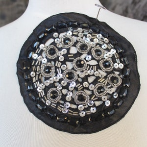 May include: A black and silver circular fabric applique with sequins and beads.