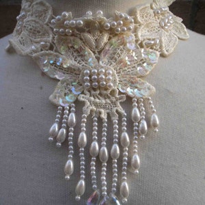 Könnte beinhalten: Eine weiße Spitzen-Choker-Halskette mit Perlen- und schimmernden Pailletten-Verzierungen. Die Halskette hat ein langes, herabhängendes Design mit mehreren Perlensträngen.