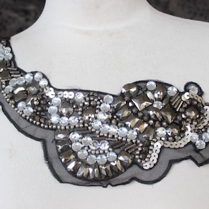 May include: A black mesh applique with silver and clear rhinestones, beads, and sequins. The applique is shaped like a curved line and is perfect for adding a touch of sparkle to clothing or accessories.