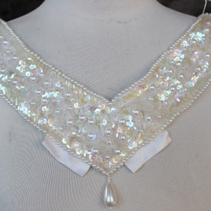 Puede incluir: Un collar blanco de lentejuelas y perlas con un colgante de perla en forma de lágrima.