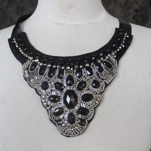 May include: A black choker necklace with silver and black bead embellishments. The necklace is in the shape of a teardrop and has a floral design in the center.