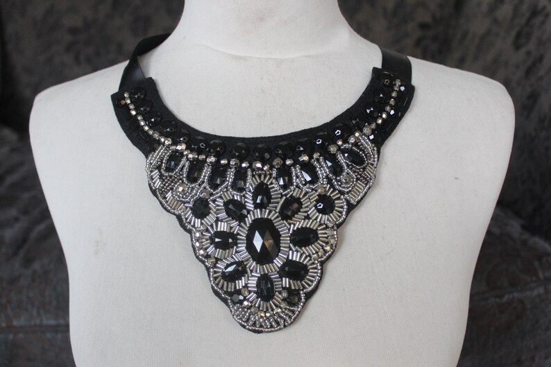 May include: A black choker necklace with silver and black bead embellishments. The necklace is in the shape of a teardrop and has a floral design in the center.