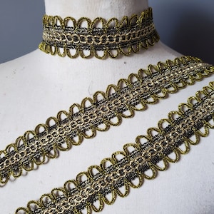 Puede incluir: Un adorno decorativo dorado y negro y un collar gargantilla a juego. El adorno y la gargantilla presentan un dise&ntilde;o de borde festoneado con un patr&oacute;n de cadena en el centro. El adorno se muestra en un maniqu&iacute;.