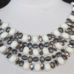 May include: A white and black beaded necklace with a scalloped design. The necklace is made of oval-shaped beads and is perfect for adding a touch of elegance to any outfit.