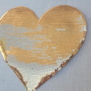 May include: A heart-shaped sequin design in gold and silver. The sequins are arranged to create a shimmering effect. The heart is a decorative item, possibly for crafts or embellishment.