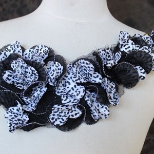 May include: Black and white leopard print fabric flower embellishment with a ruffled design. The fabric is layered and has a sheer black mesh overlay.