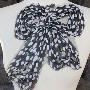 May include: A large black and white polka dot bow made of sheer fabric. The bow is decorated with black beads.