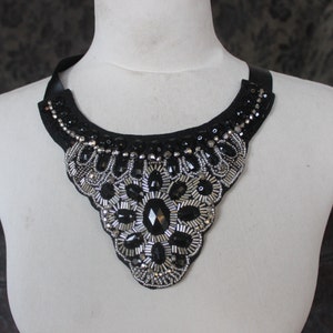 May include: A black choker necklace with silver and black bead embellishments. The necklace is in the shape of a teardrop and has a scalloped edge.