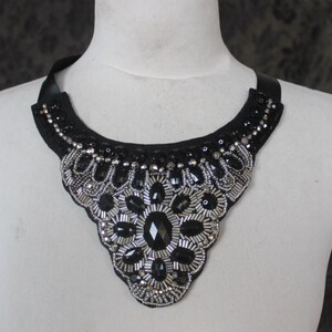 May include: A black and silver beaded statement necklace with a large, ornate design. The necklace is made of black fabric with silver beads and sequins.