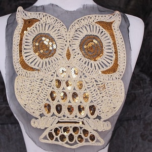 May include: Gold and white sequined owl applique on a black mesh background. The owl is detailed with a white outline and gold sequins.
