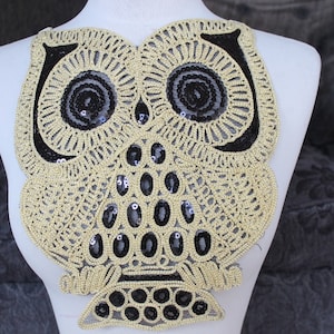 May include: A gold and black owl-shaped applique with sequins. The owl has large eyes and a detailed design.