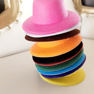 Puede incluir: Una pila de sombreros de fieltro de colores en varios tamaños, incluyendo rosa, blanco, marrón, naranja, negro, verde, azul, morado y amarillo.