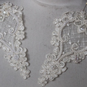 May include: Two ivory lace appliques with pearl beading and a delicate floral design. The appliques are perfect for adding a touch of elegance to any project.