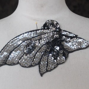 May include: Silver sequin butterfly applique with black bead accents. This embellishment is perfect for adding a touch of sparkle to clothing, bags, or home decor projects.