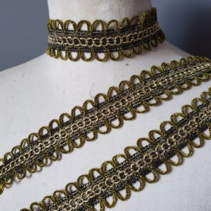 Puede incluir: Un conjunto de adornos y gargantilla decorativos dorados y negros. El adorno presenta un borde festoneado con un dise&ntilde;o en forma de cadena. La gargantilla es una pieza a juego. El conjunto se muestra en un maniqu&iacute;.