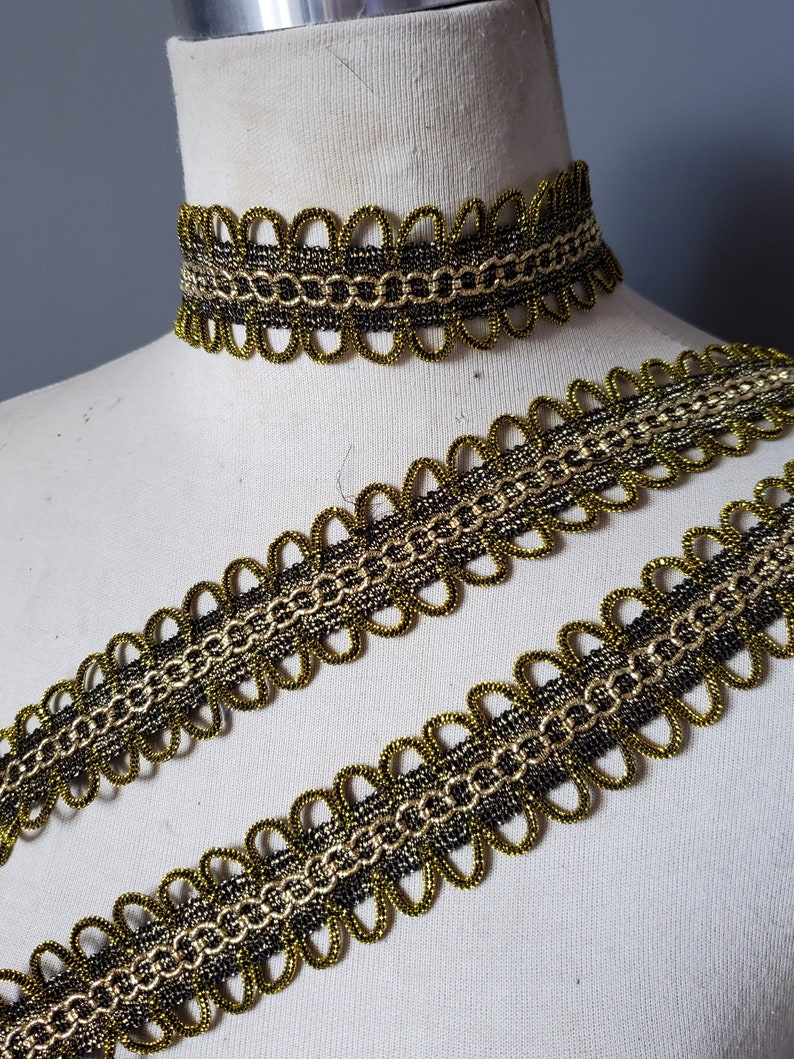 Puede incluir: Un conjunto de adornos y gargantilla decorativos dorados y negros. El adorno presenta un borde festoneado con un dise&ntilde;o en forma de cadena. La gargantilla es una pieza a juego. El conjunto se muestra en un maniqu&iacute;.
