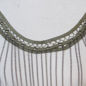 Puede incluir: Un collar choker de tela verde con flecos de cadena. La tela tiene un delicado patrón de encaje y está adornada con cuentas plateadas.