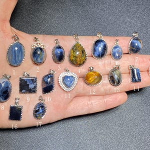 Puede incluir: Una colección de colgantes de piedras preciosas en varias formas, incluyendo ovaladas, de lágrima y cuadradas. Los colgantes presentan tonos azules y dorados, engastados en metal plateado. Algunos tienen diseños intrincados, otros son simples.